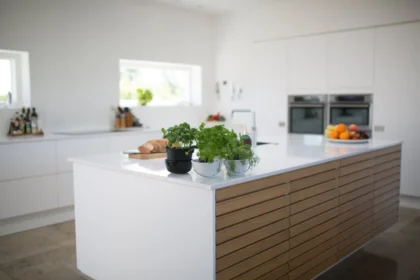 Een keuken met strak wit design met op de voorgrond een aantal kruiden in potten en op de achtergrond een fruitschaal en aangesneden brood.