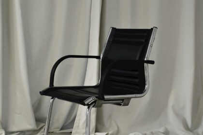 Een moderne zwarte stoel, geplaatst voor een wit gordijn.